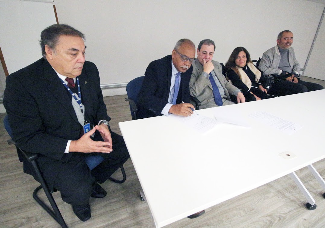 cinco pessoas na foto, atrás de uma mesa. Um dos representantes da ABNT assina o termo. 